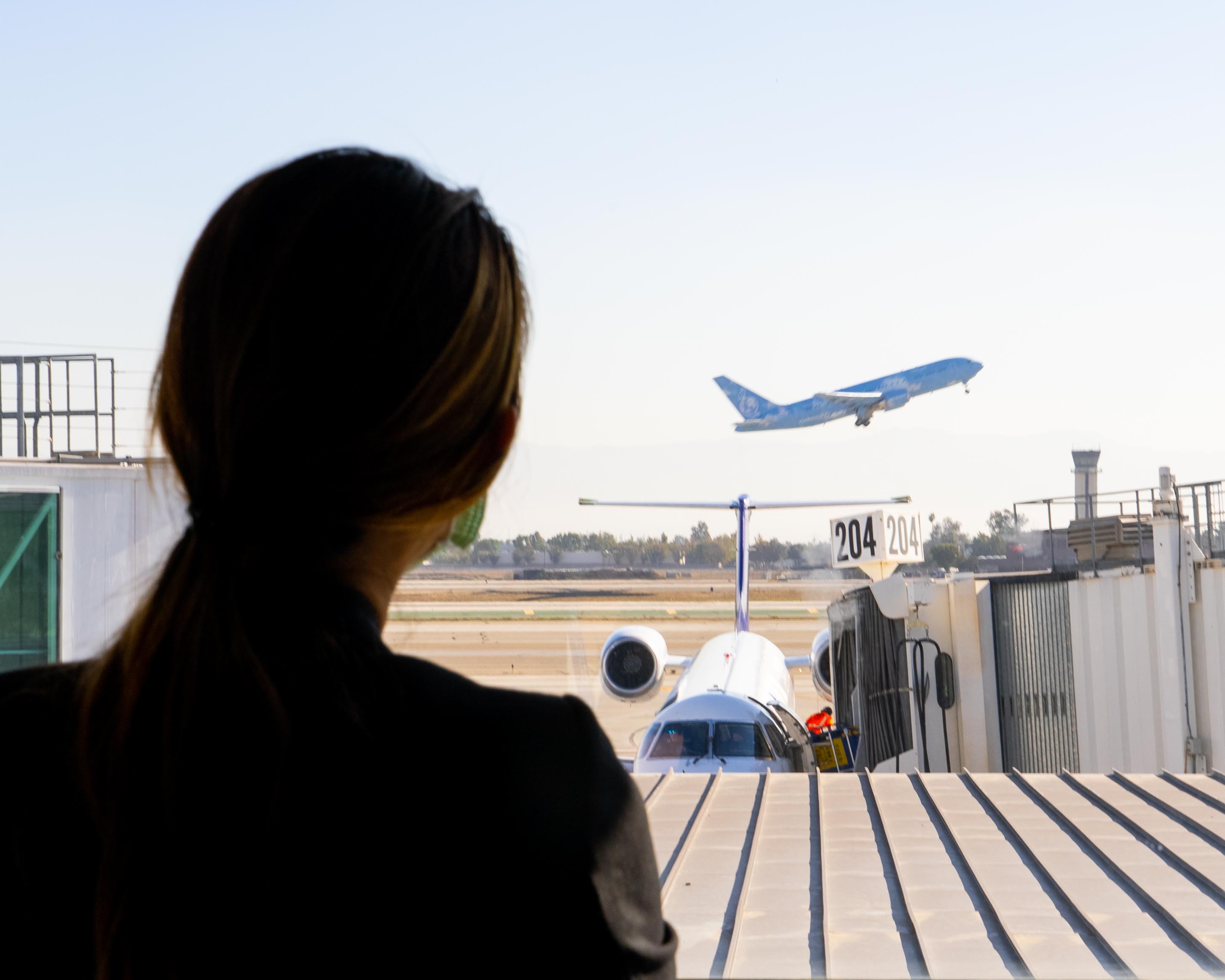 woman looking out window at plane taking off at ONT Airport