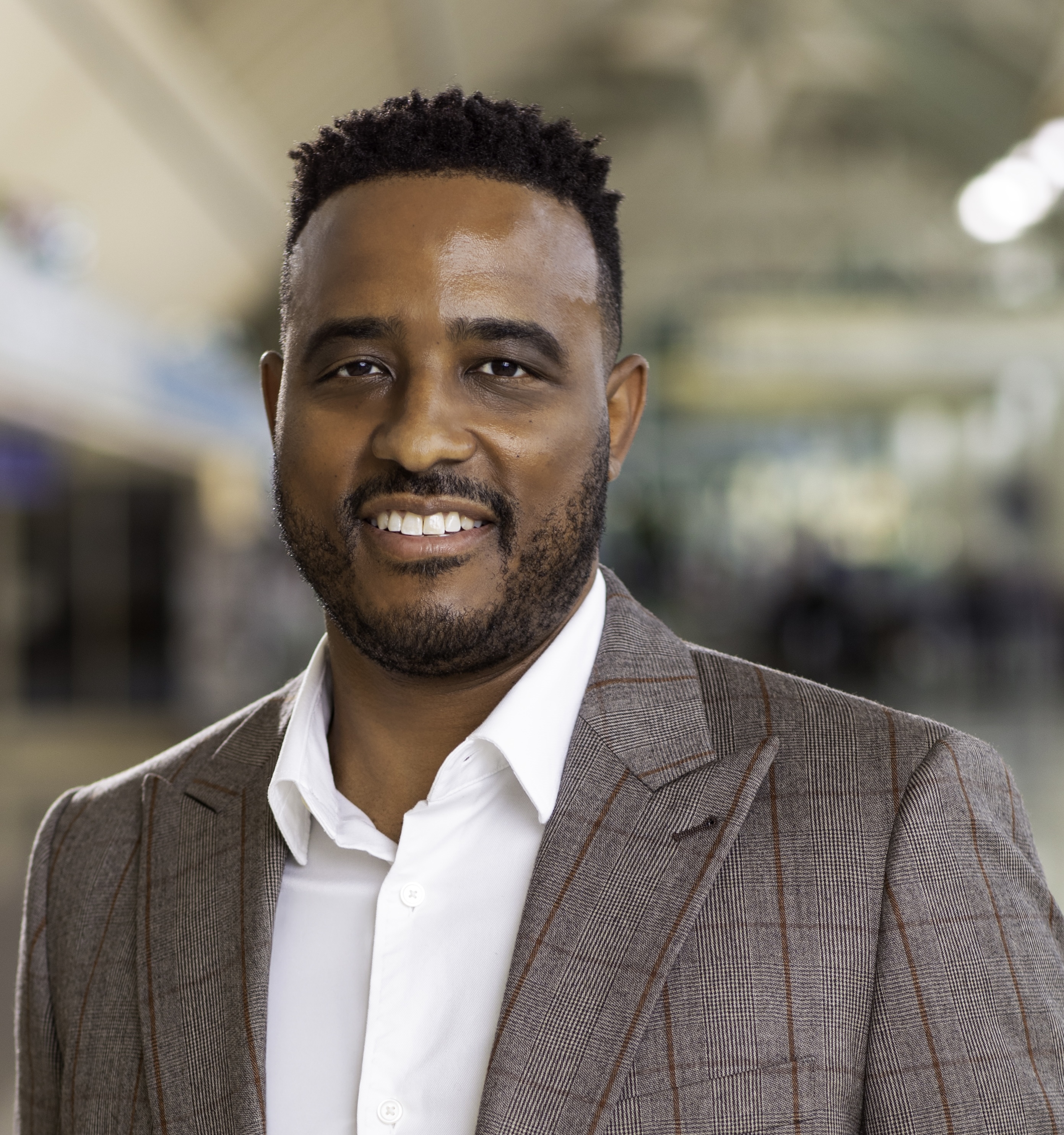 Jamal Avilez in gray suit jacket with blurred office background.