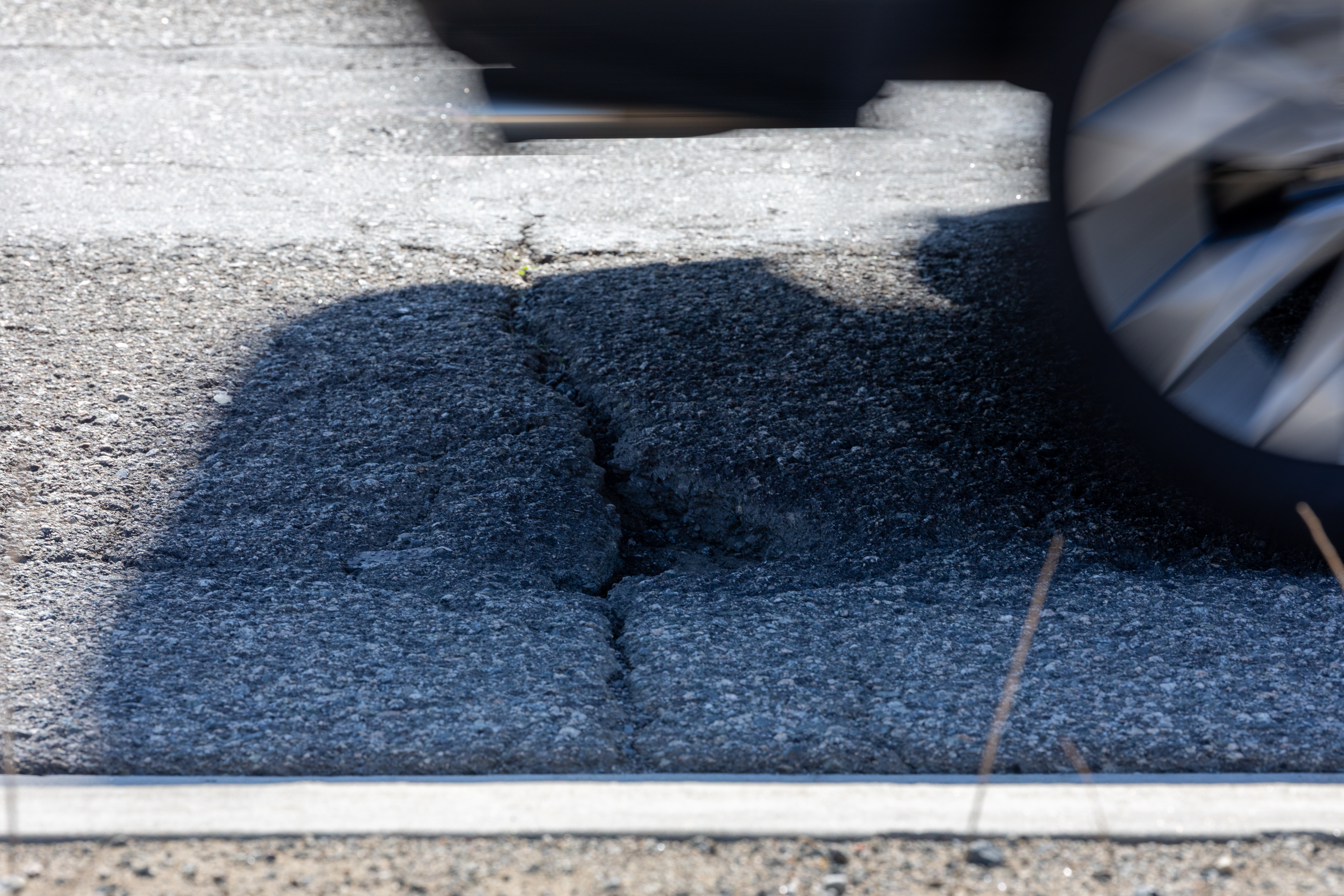 Fresh asphalt with repair line and partial view of vehicle tire.