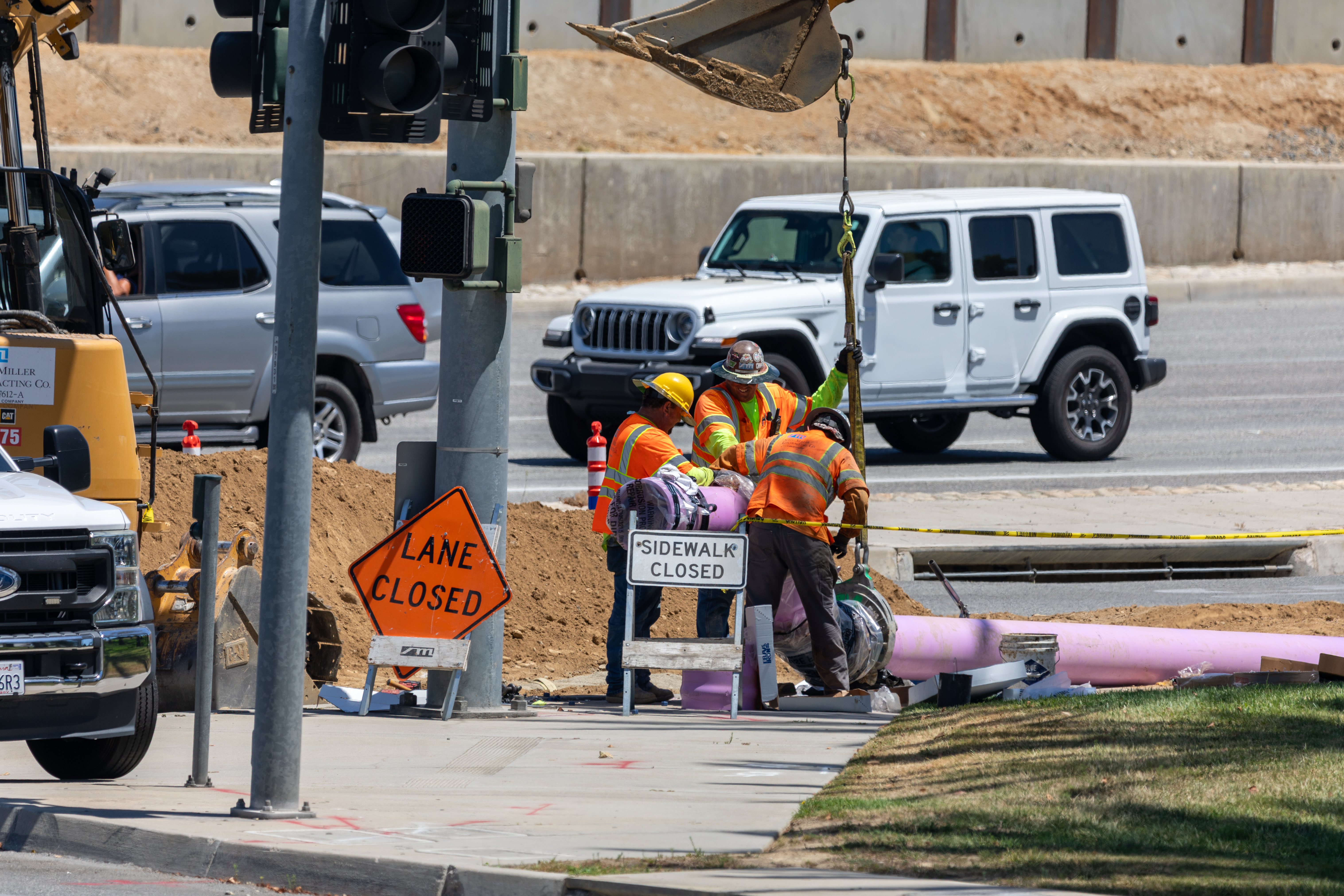 Road construction workers in orange vests working at an intersection with white vehicles nearby.