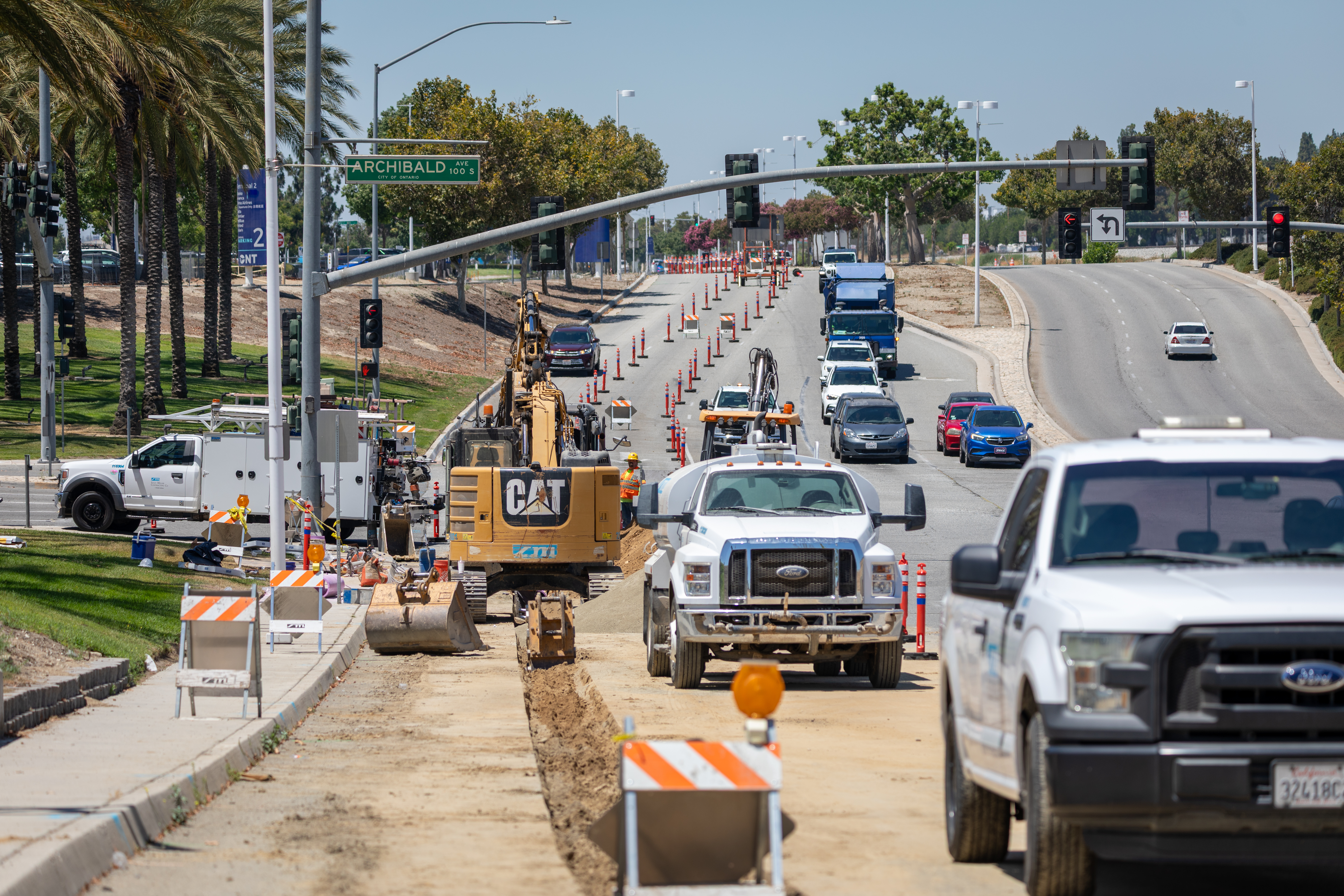 Construction of a light rail line alongside a busy highway with traffic and palm trees.