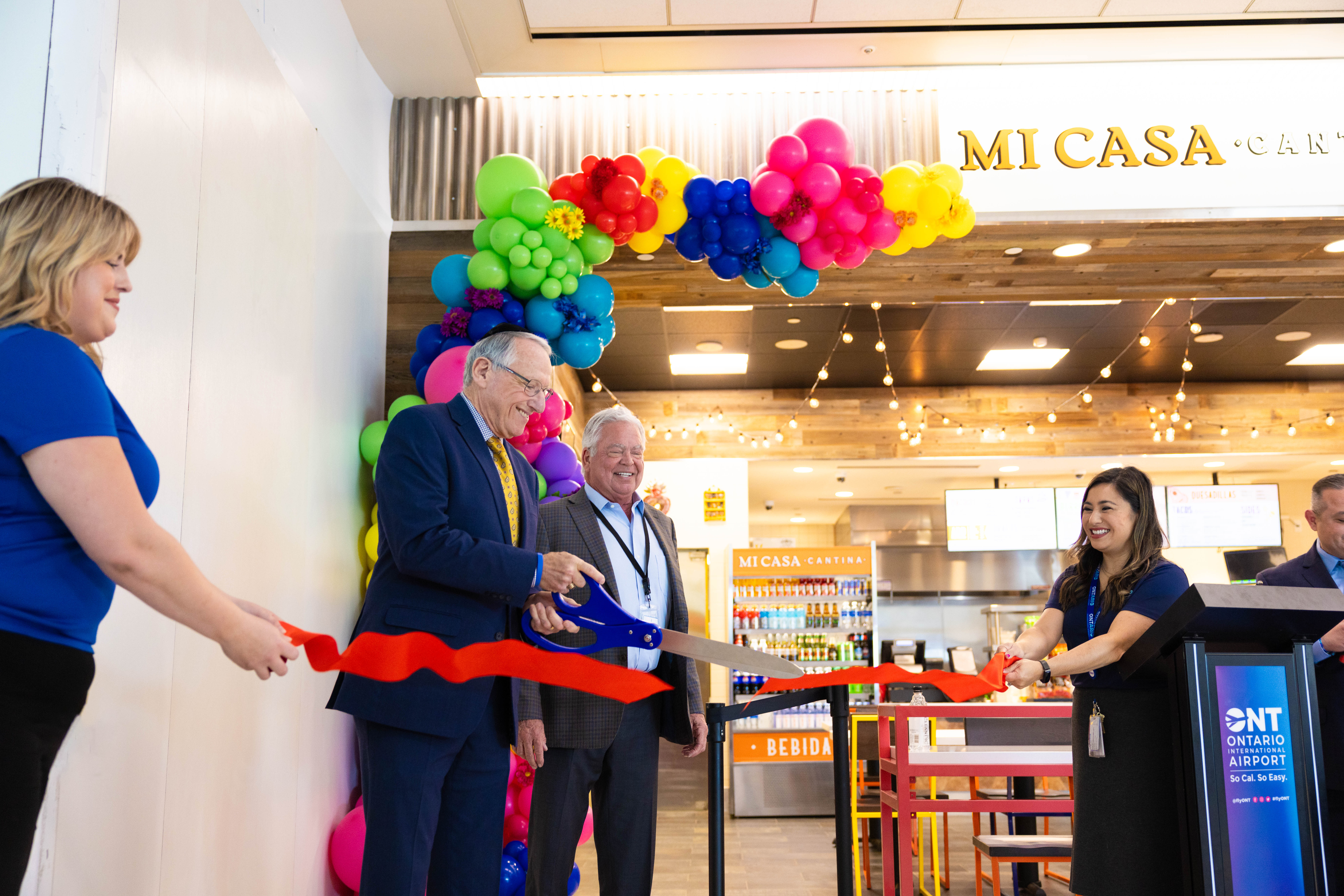 Person in colorful sombrero cutting a red ribbon at a restaurant grand opening ceremony.