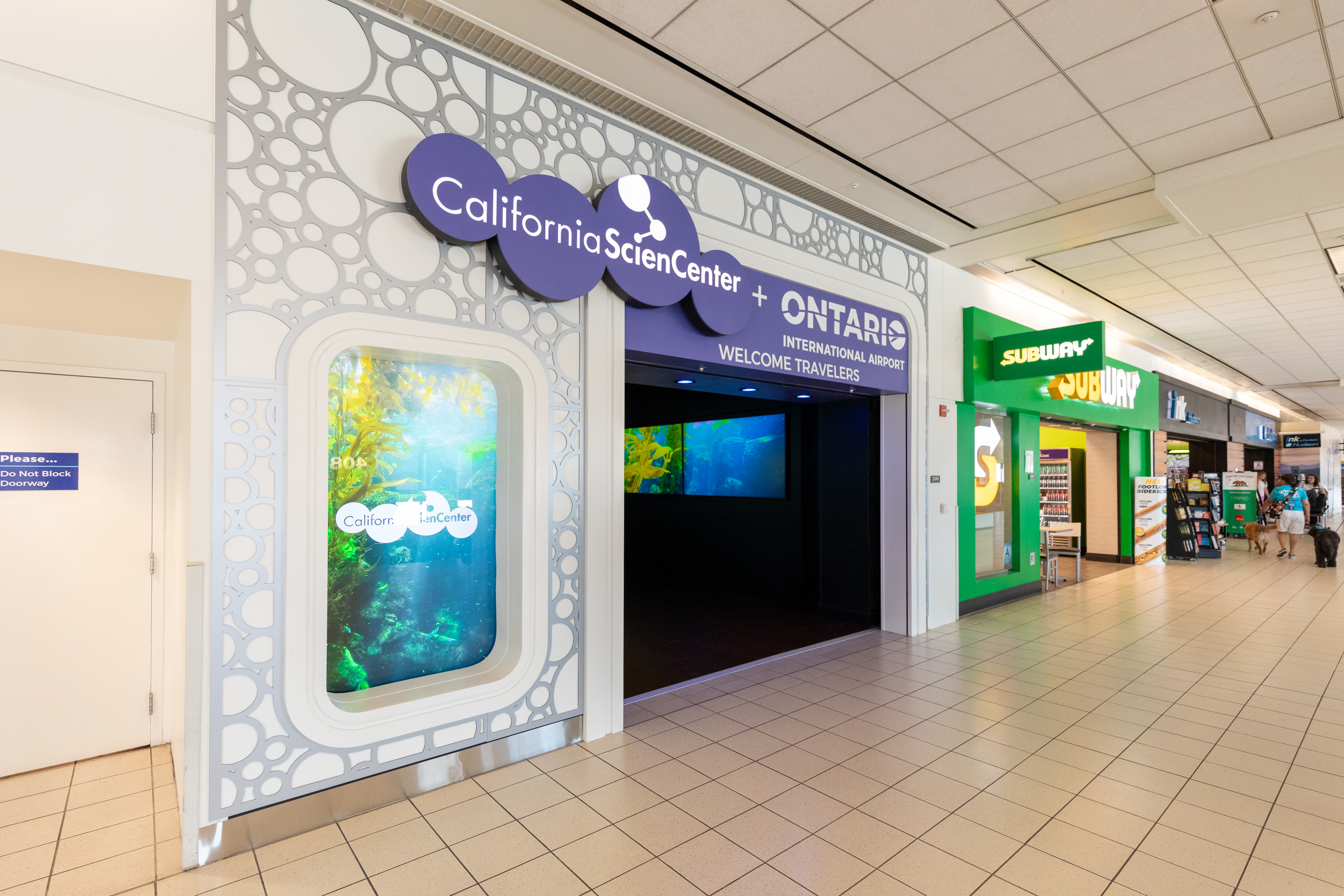 Storefronts in a shopping mall corridor with colorful retail displays and signage.