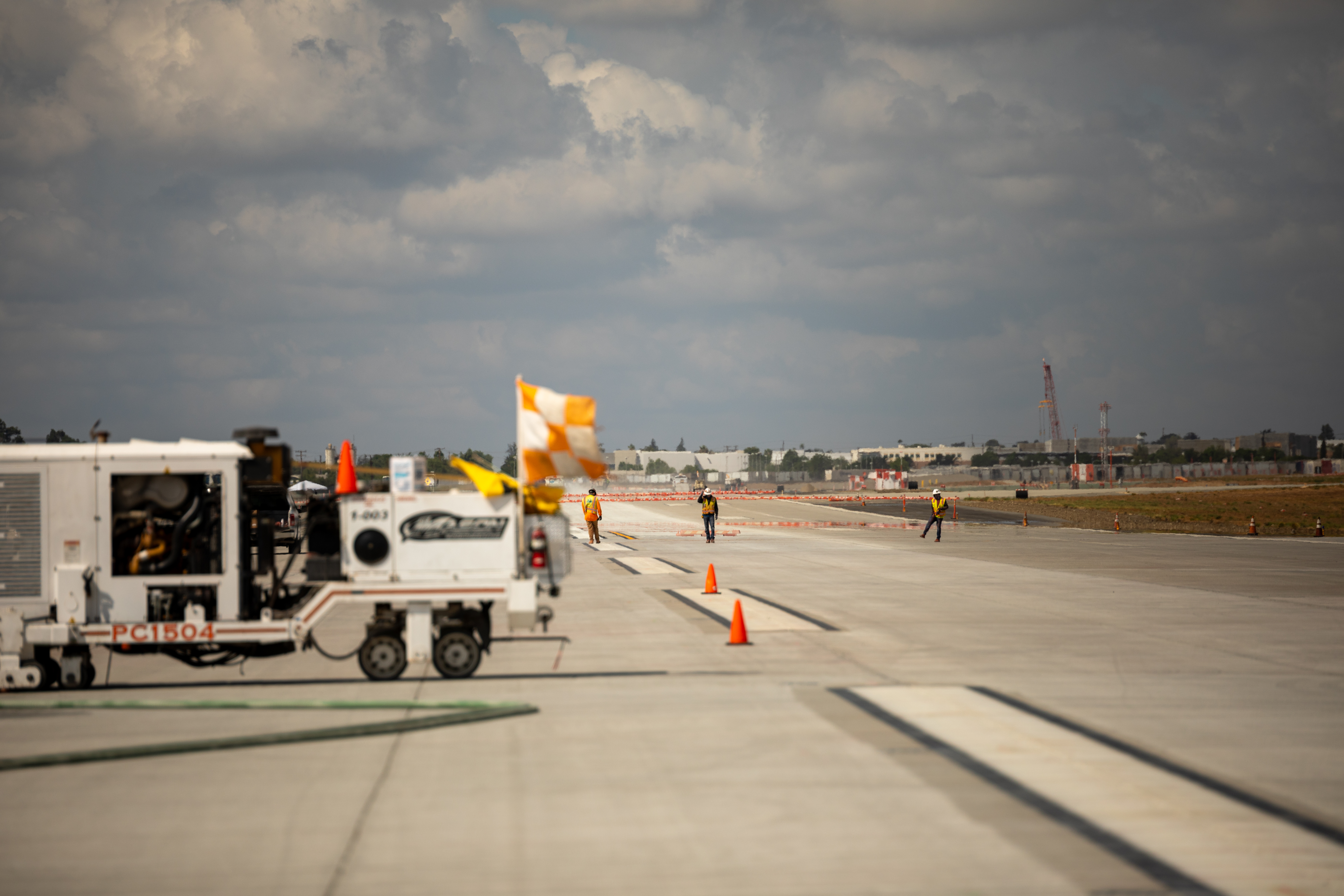 Airport tarmac with ground service equipment and runway under cloudy sky.