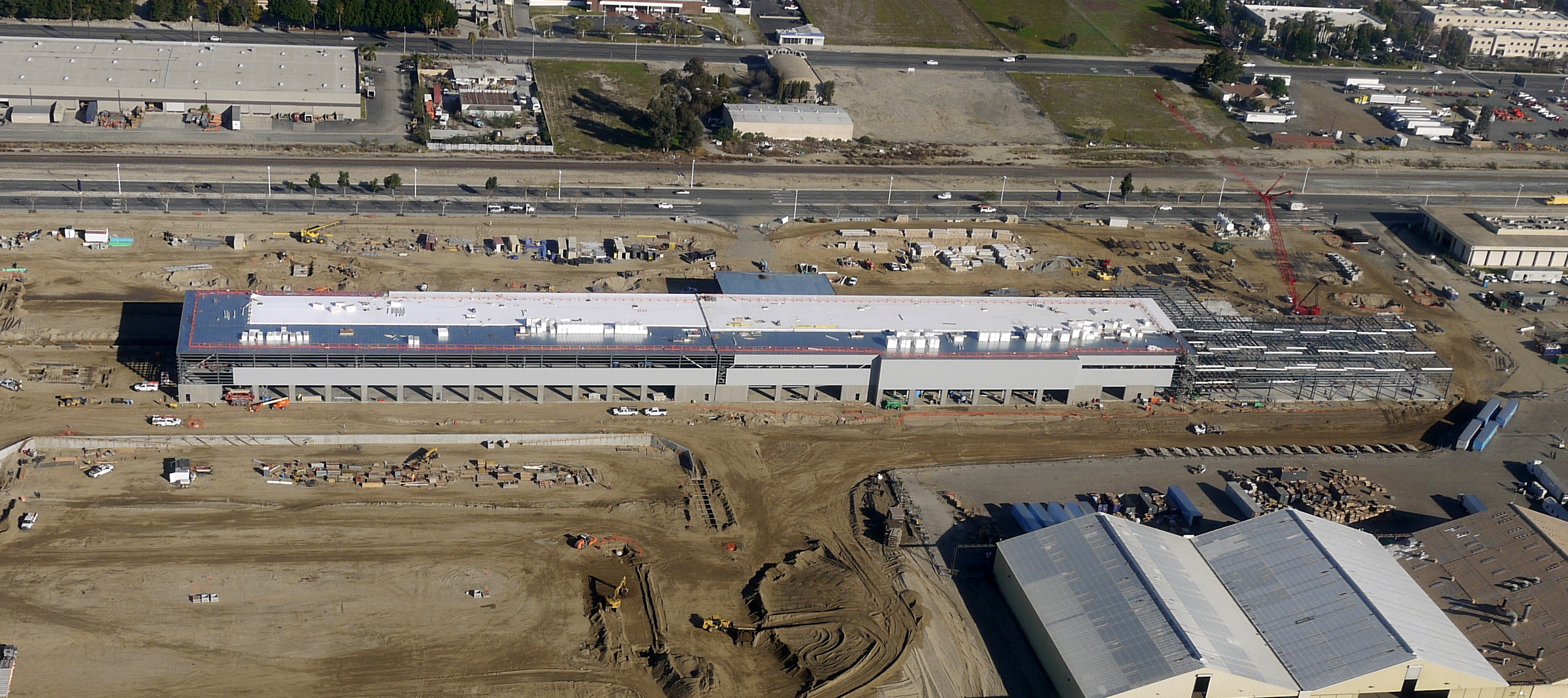 Aerial view of industrial area with long white warehouse buildings and surrounding infrastructure.