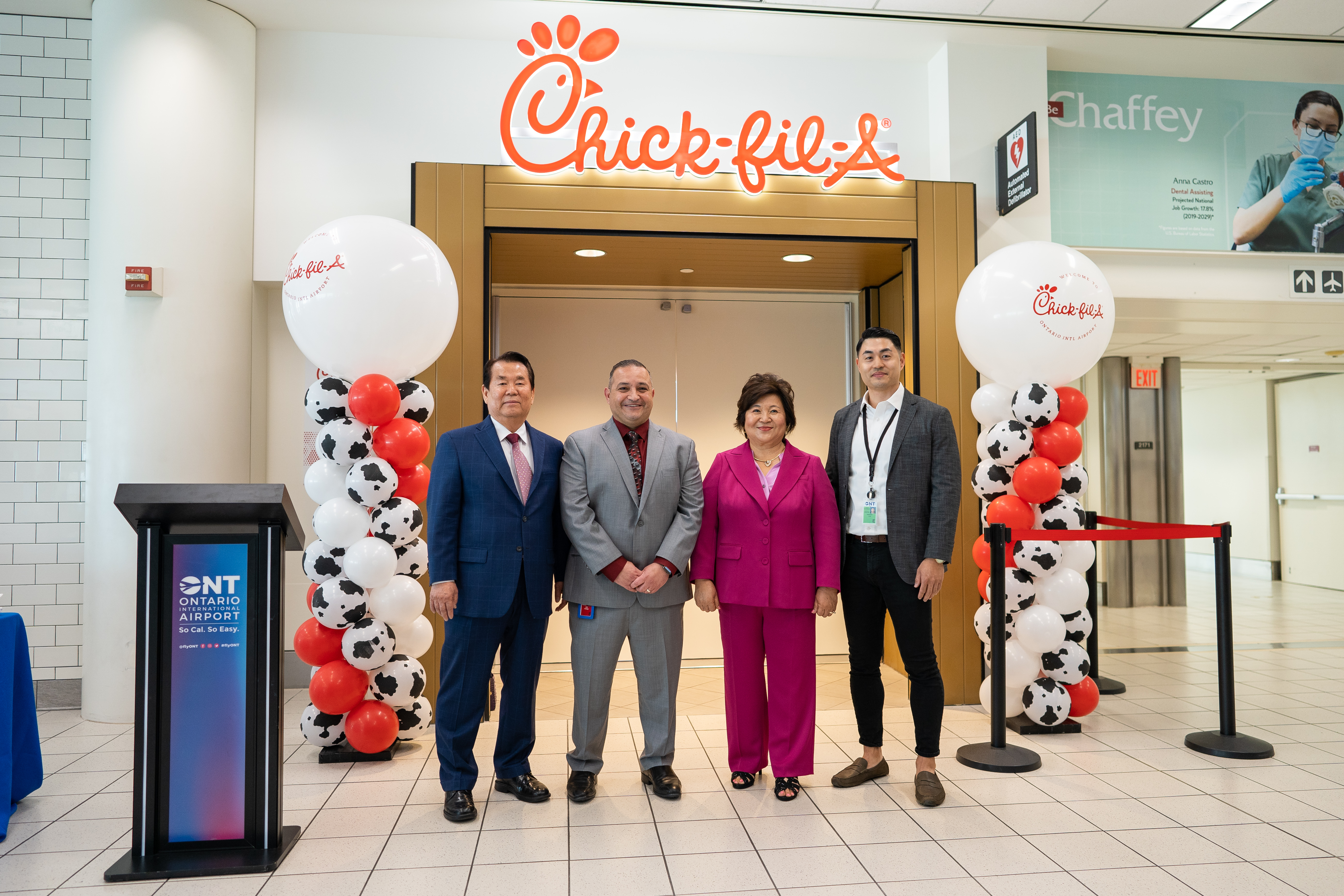 Four people in formal attire standing in front of a Chick-fil-A restaurant with balloon decorations.