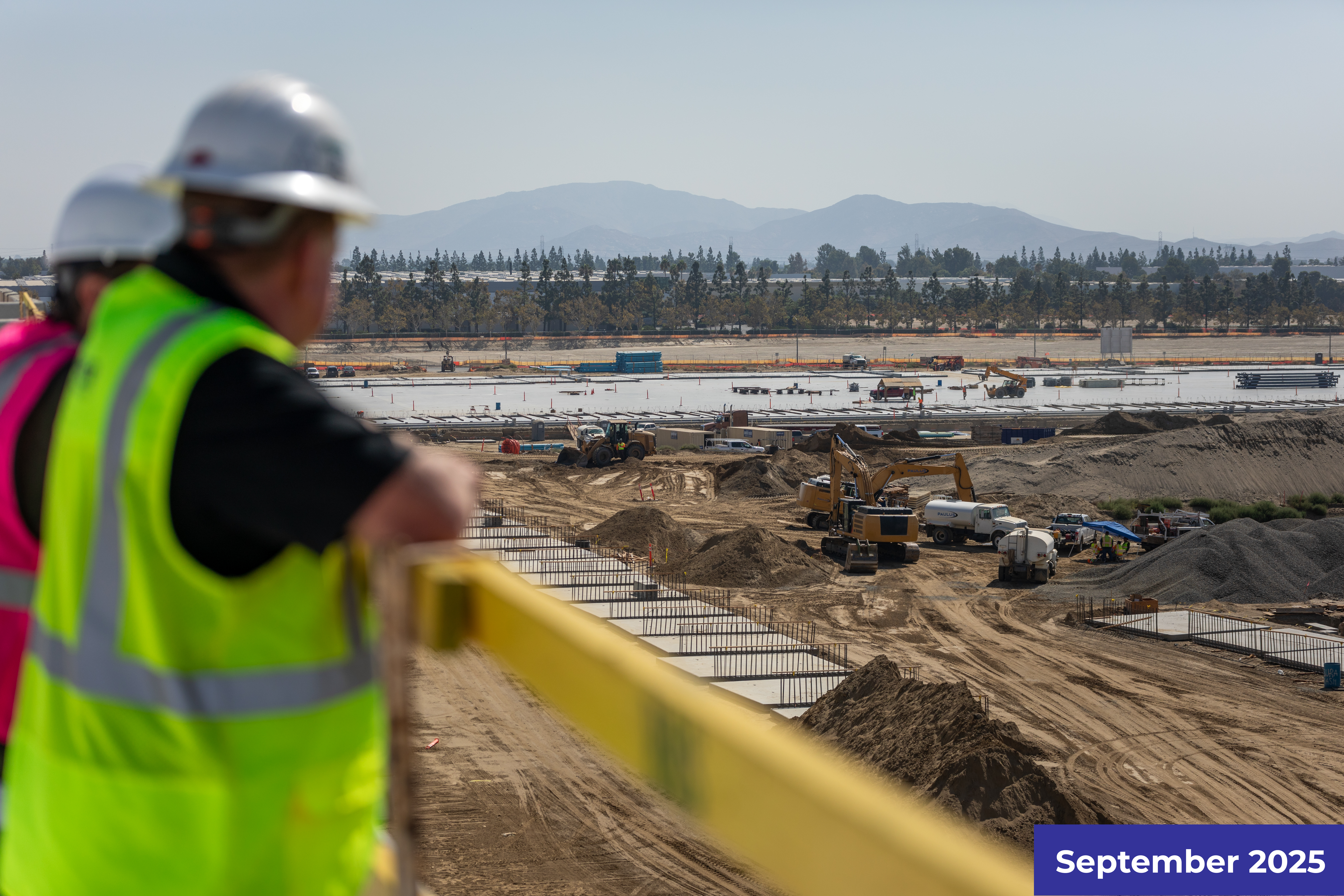 Construction worker in safety gear overlooking a large development site with earthworks.