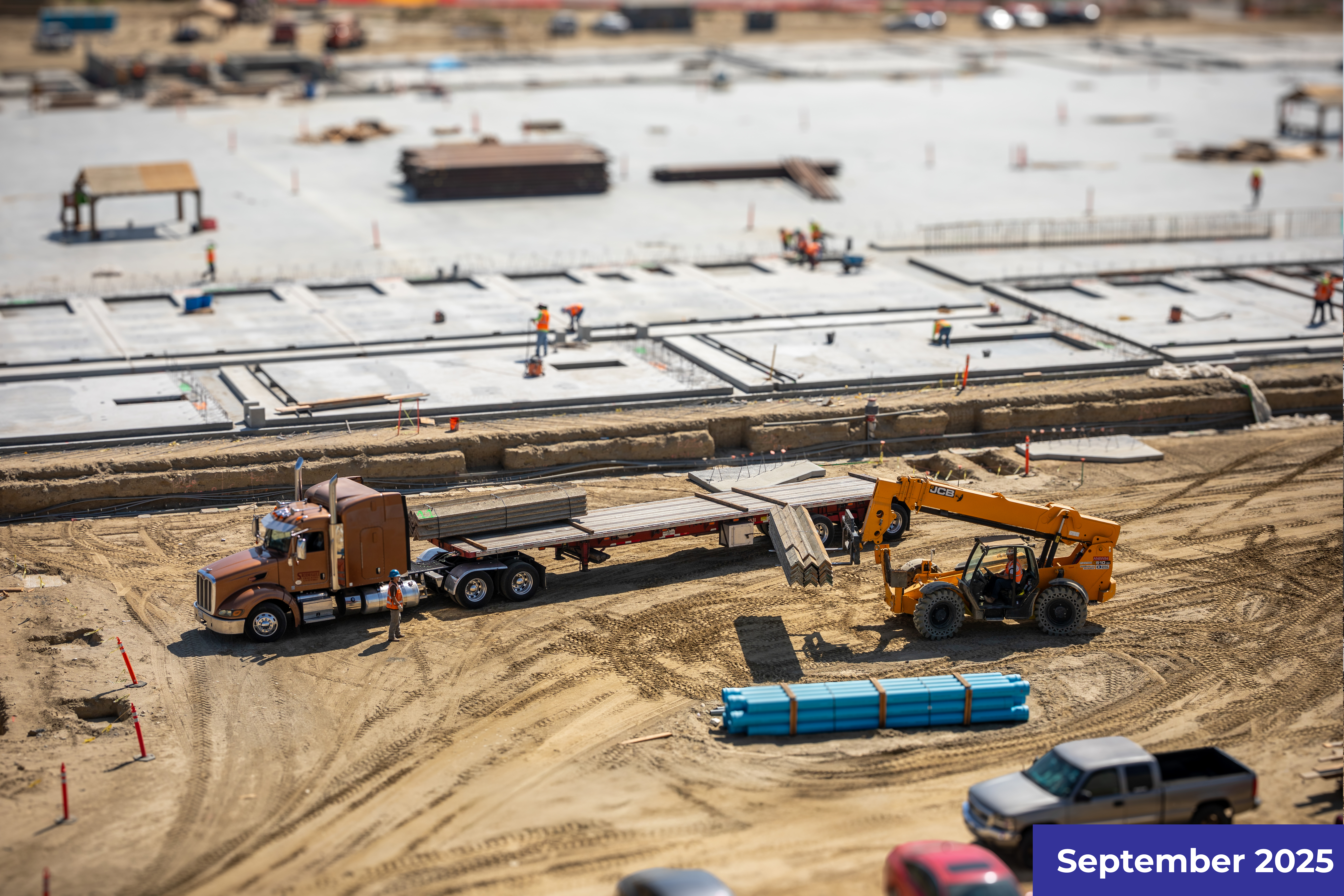 Construction site with heavy machinery, yellow trucks, and prefabricated concrete elements being installed.