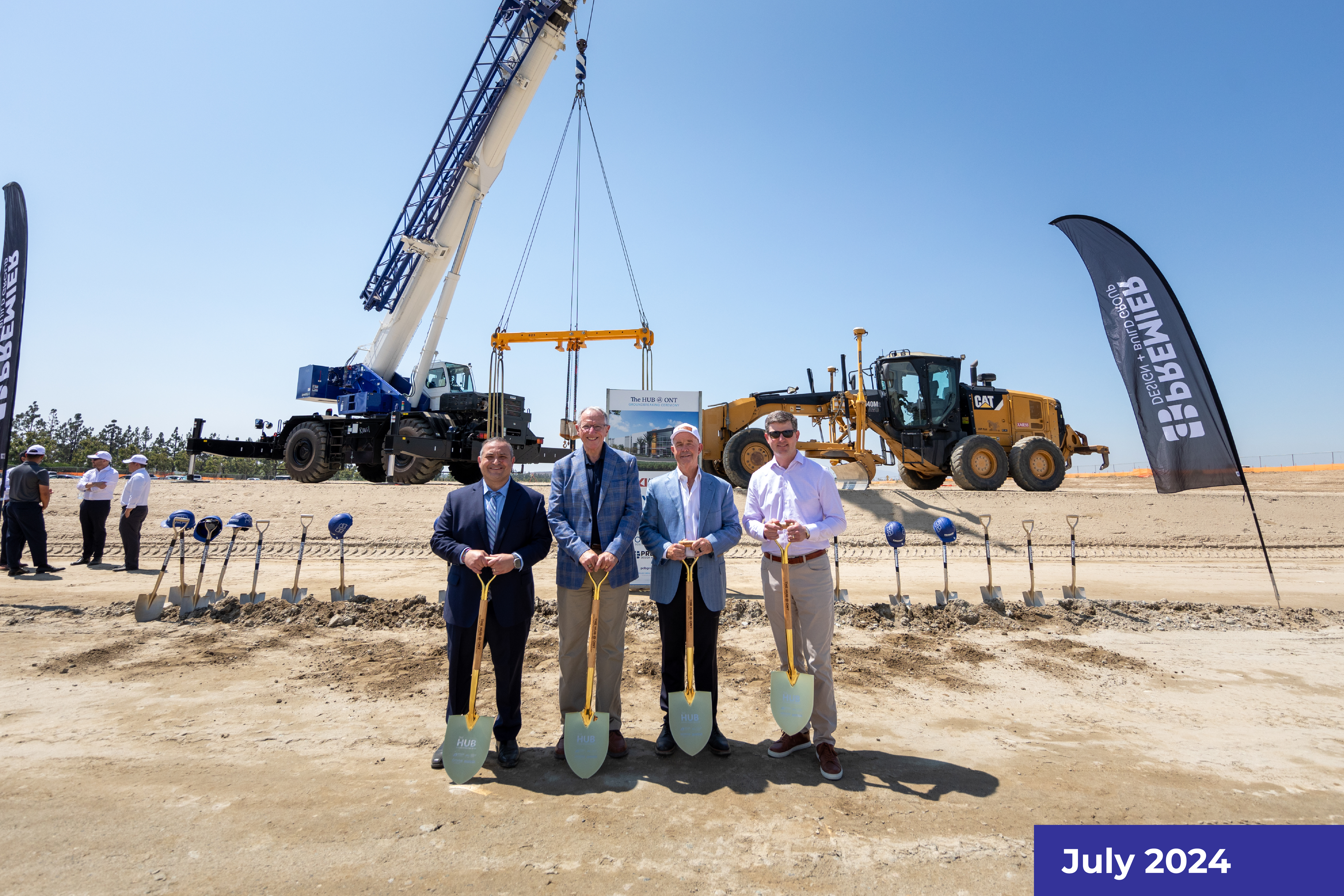 Four people in business attire standing at a construction site with heavy machinery in the background.