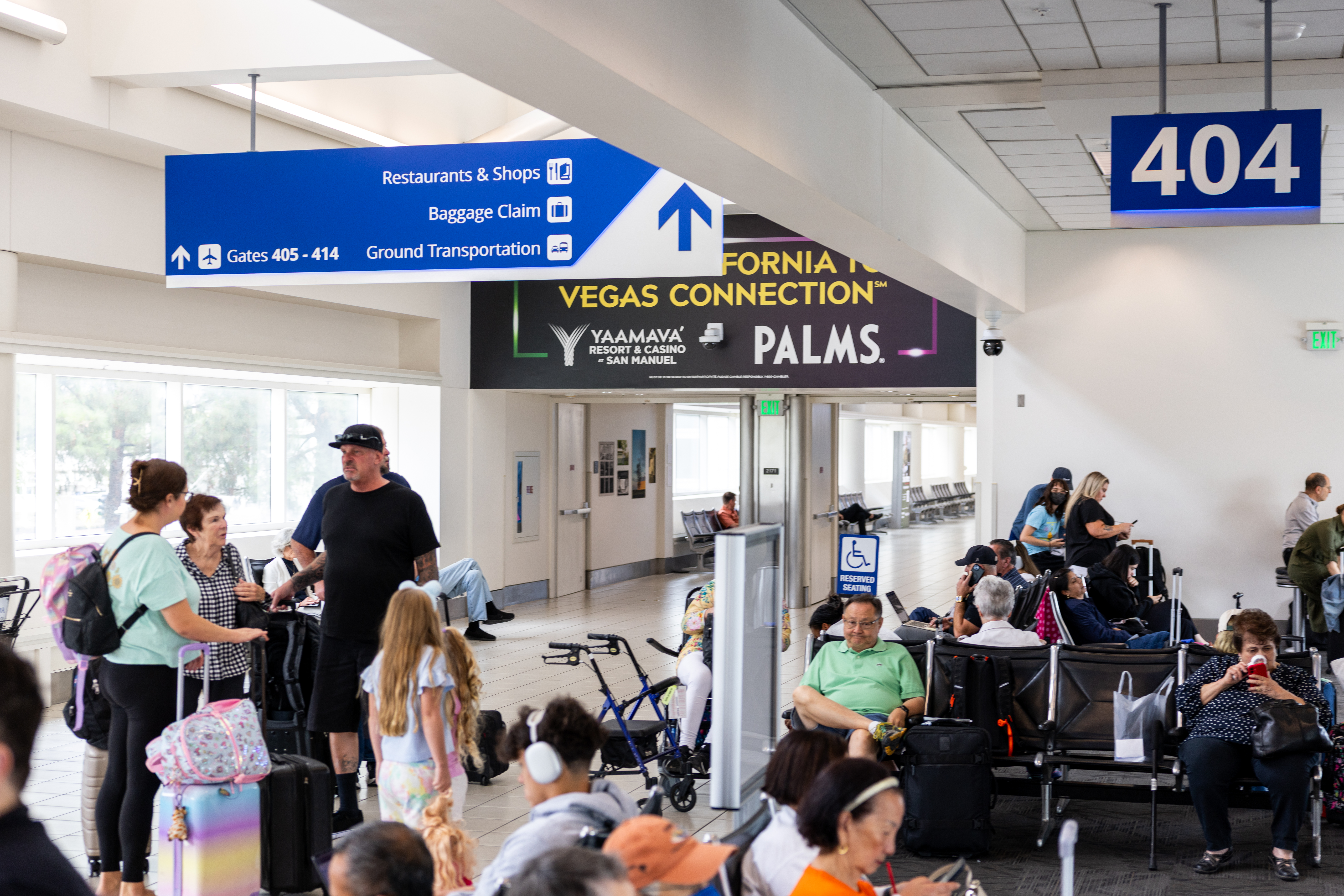 Busy airport terminal with travelers waiting at gate 404 under blue directional signs.