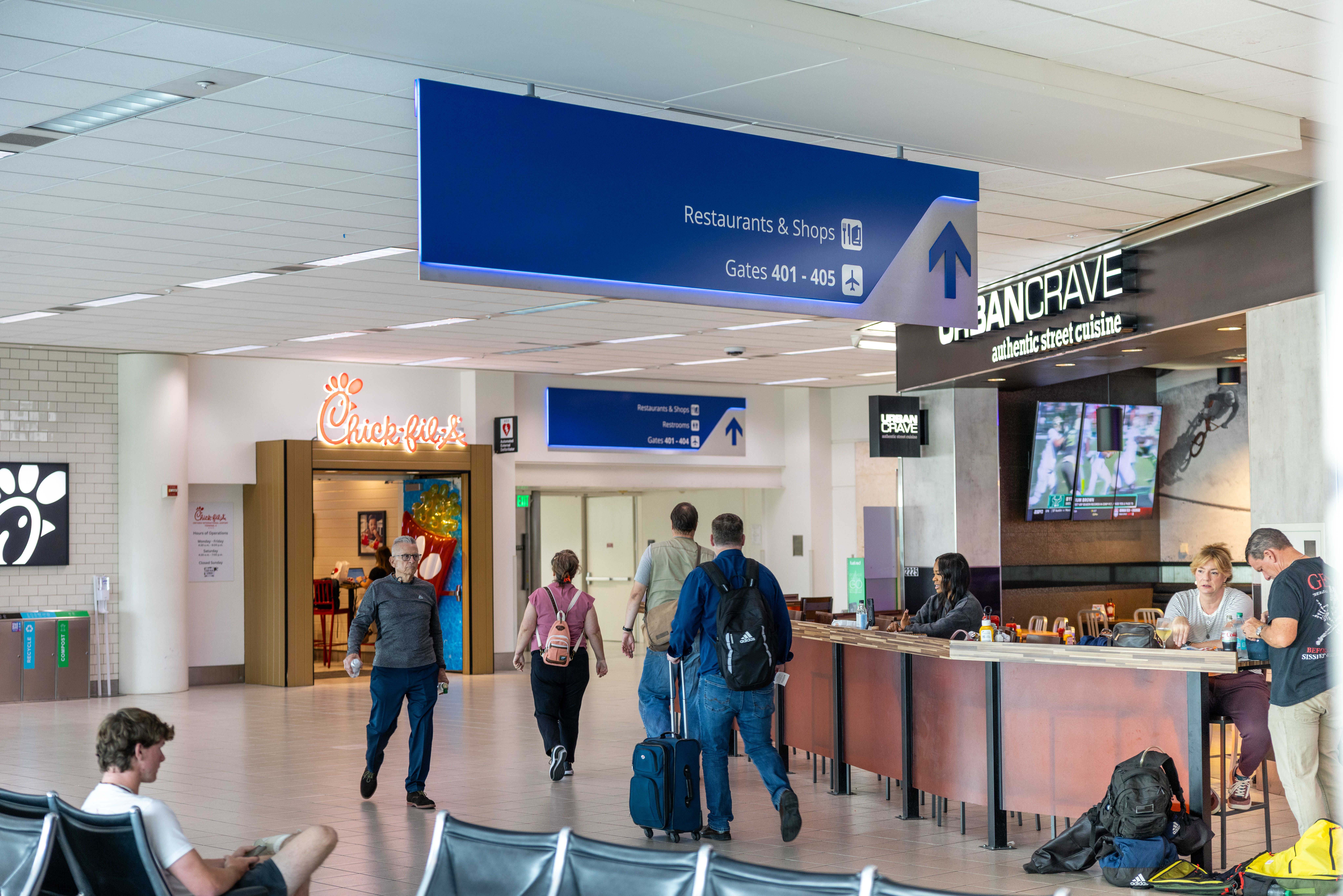 People at a hotel reception counter with blue signage above in an airport-style setting.
