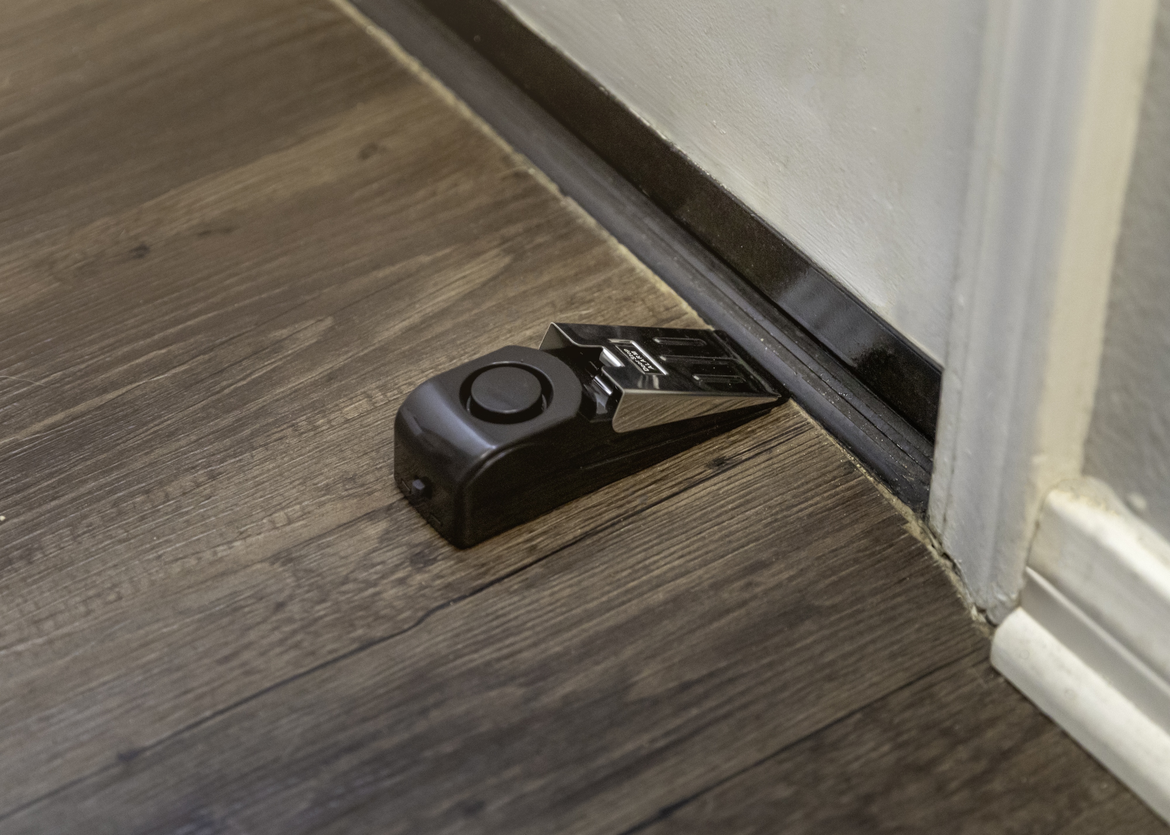 A set of keys with keychain lying on wooden floor near the baseboard of a doorway.