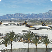 Commercial aircraft parked at an airport with mountains in the background and palm trees in foreground.