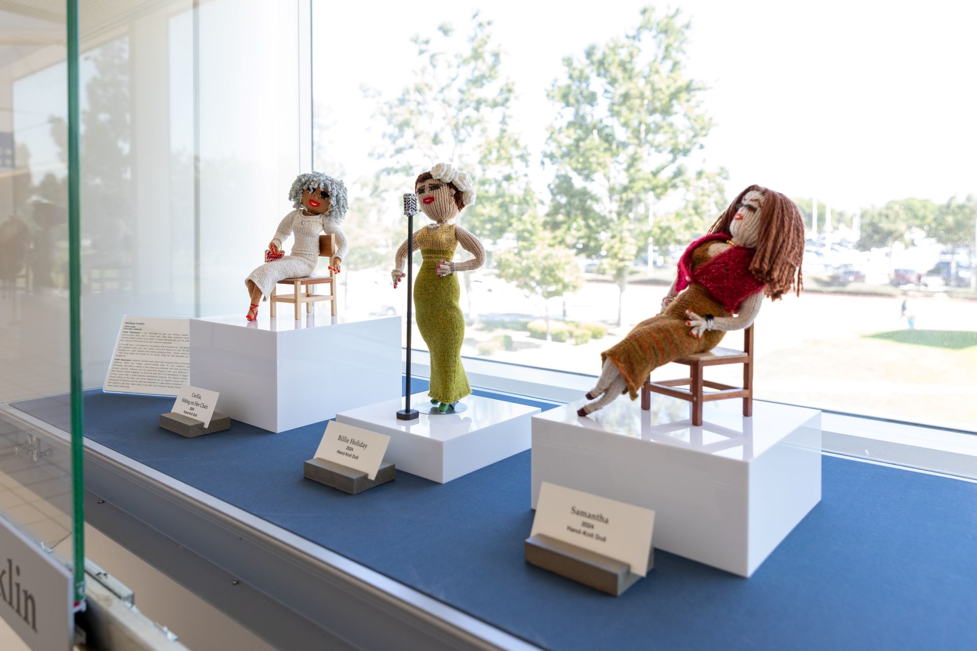 Three small woven figures of women are seen in a display case.