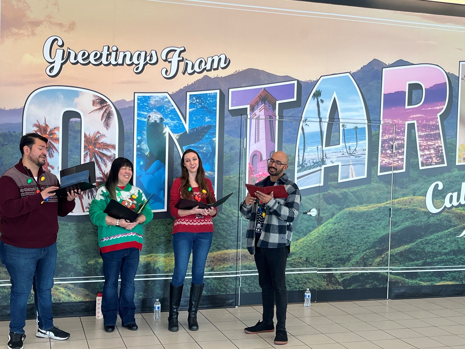 Four carolers perform in front of an Ontario mural at ONT.
