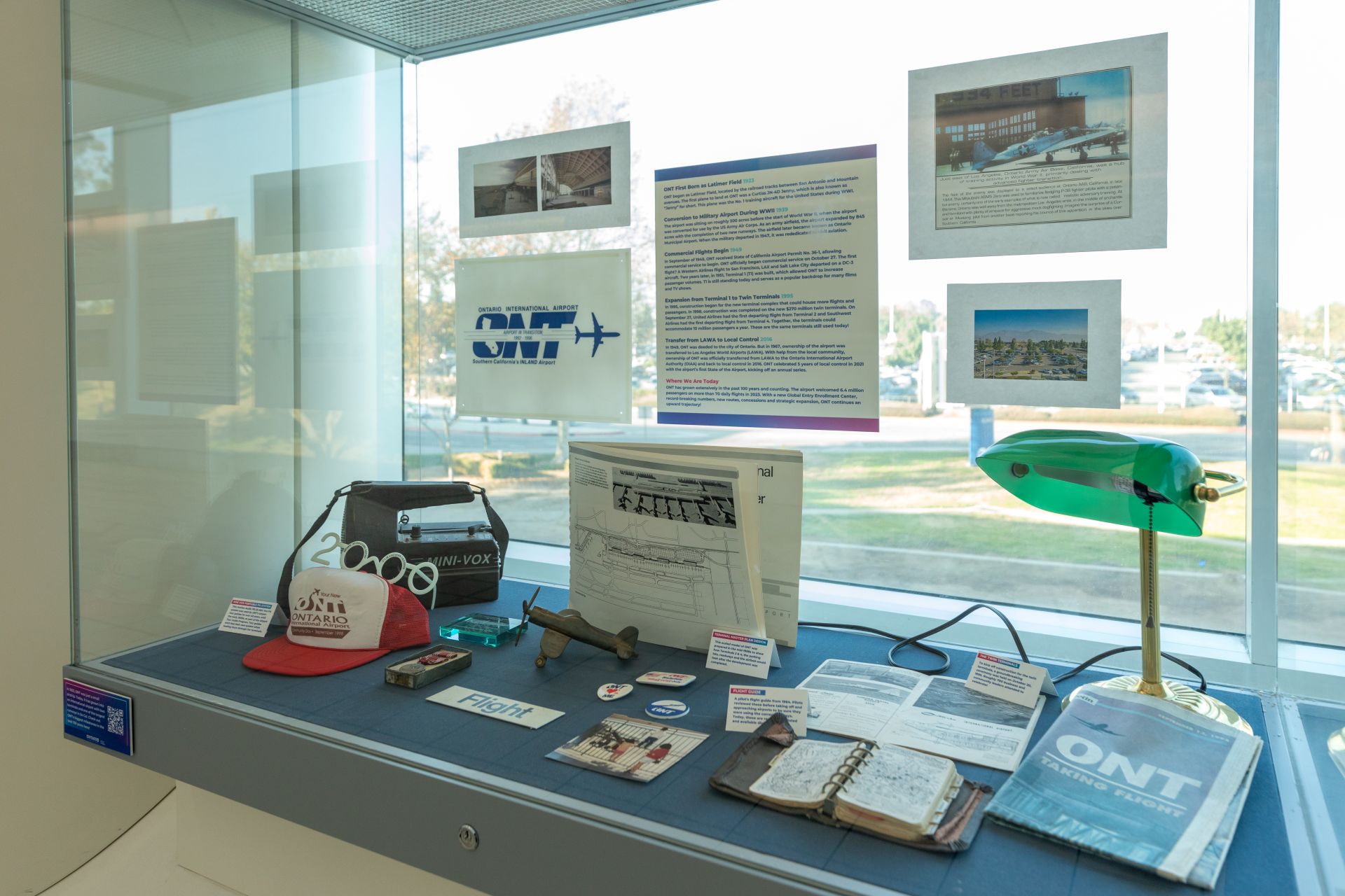A display case contains historic photos and items such as a red hat, old signage, a vintage lamp and more.
