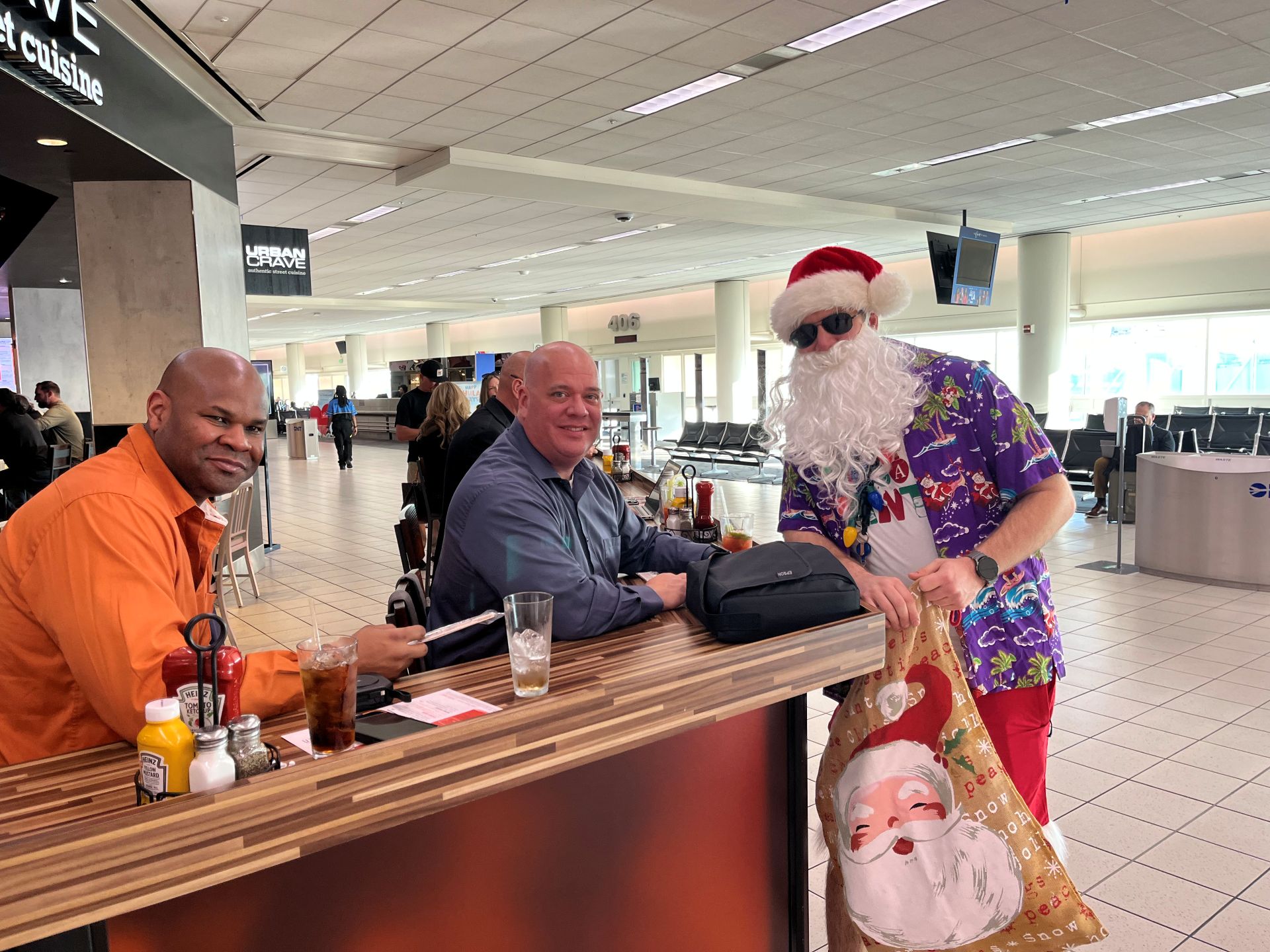 A man in shorts, a surfer shirt and Santa gear carries a bag of gifts in the terminals.