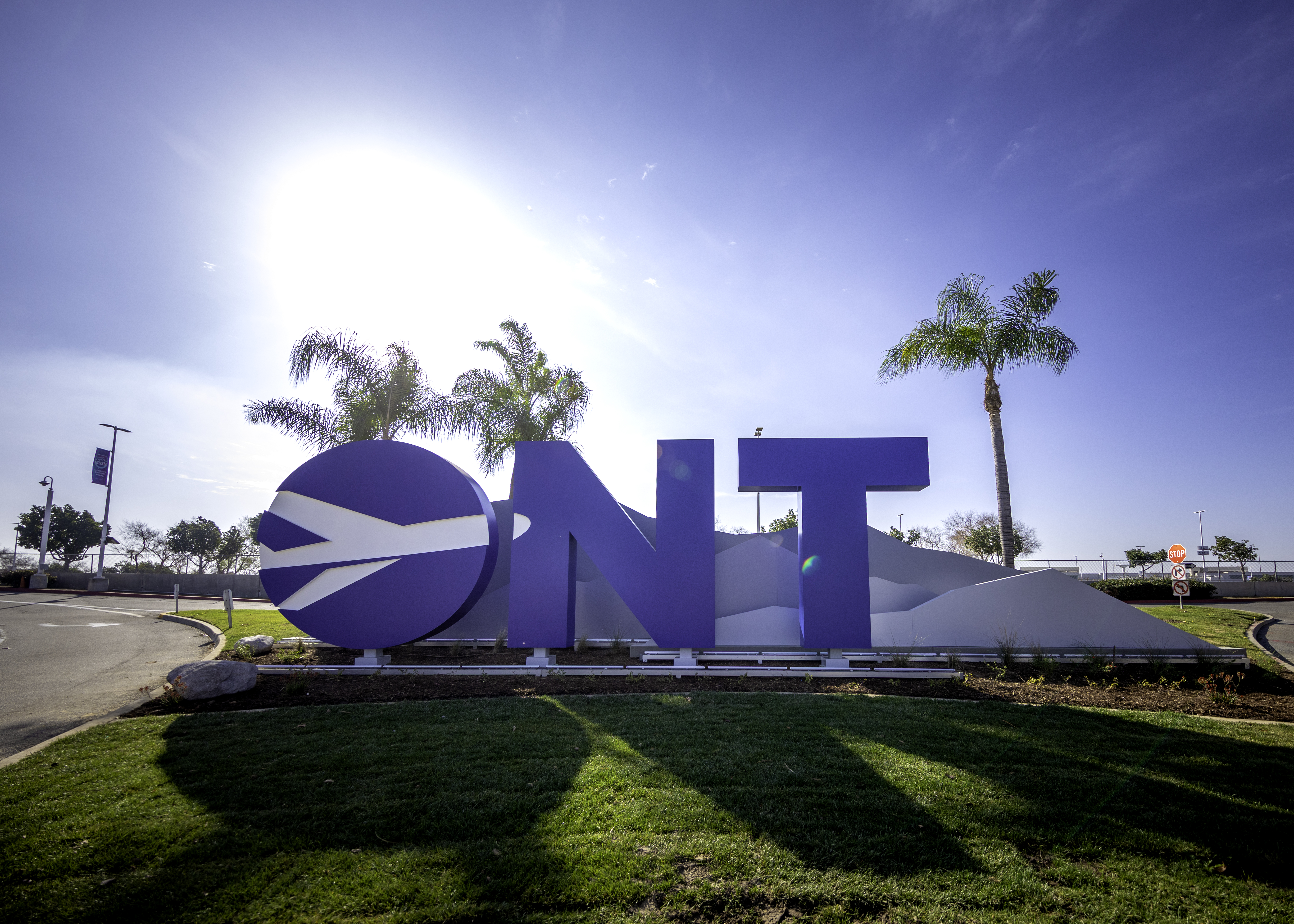 Large blue "ONT" sign with palm trees and bright sunlight at tropical location.