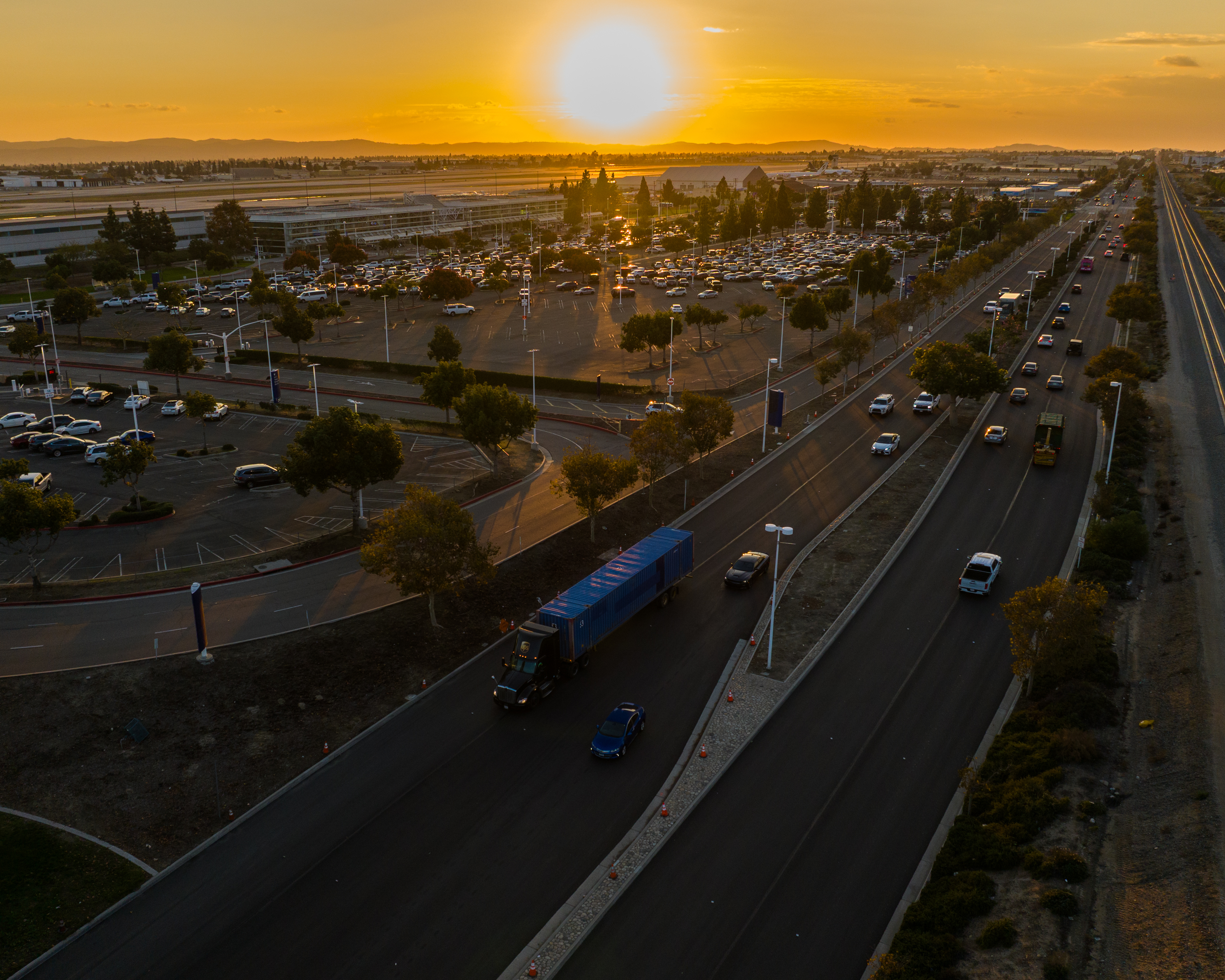 Busy highway and cityscape at sunset with golden sunlight illuminating the horizon.