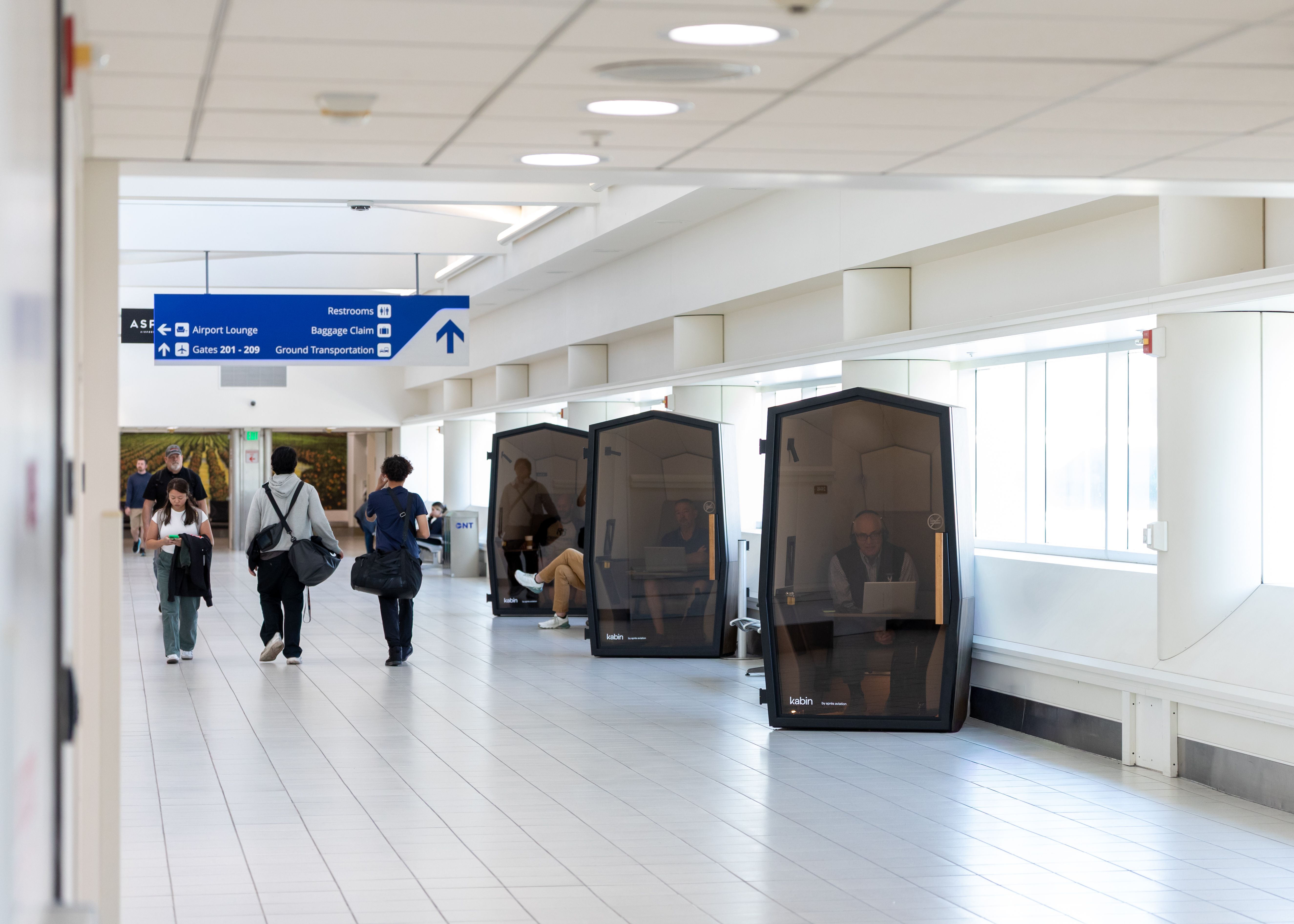 A bright, spacious airport terminal with travelers walking through the hallway.