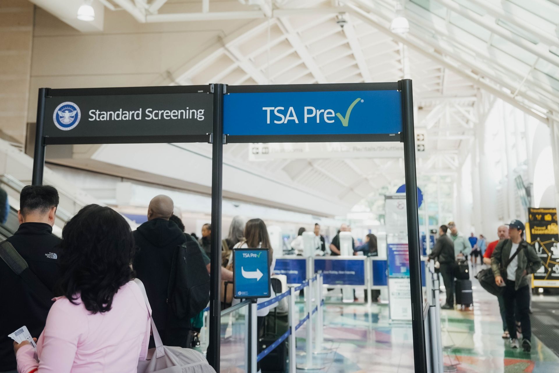 Signs say "Standard Screening" and "TSA PreCheck," with people waiting in the standard line.