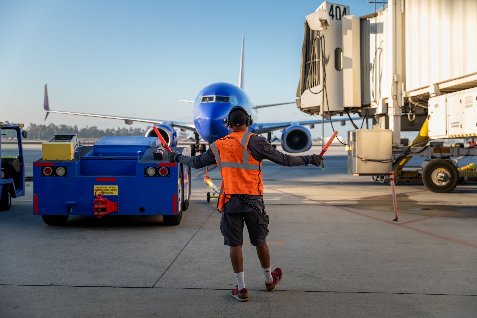 A man in a neon orange vest waves orange sticks to direct a nearby plane on the runway.