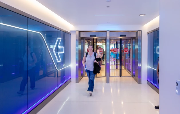 Modern exit corridor with blue glass walls and people walking through.