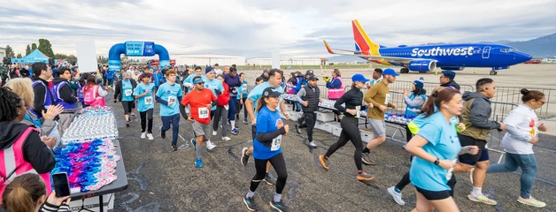 Participants running across tarmac at airport event with Southwest Airlines plane in background.