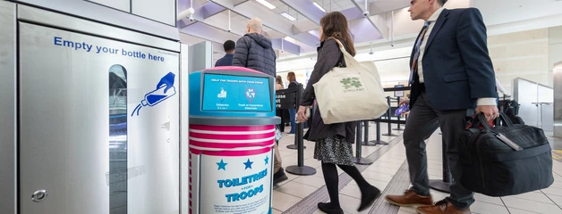 People walking past a digital information kiosk in a modern transit station.