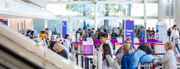 Busy airport terminal with travelers at check-in counters and colorful display screens.