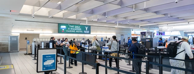 Airport check-in area with passengers in line at counters under bright lighting.