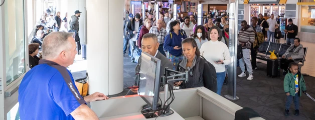 Airport security checkpoint with travelers queueing while staff monitors the process