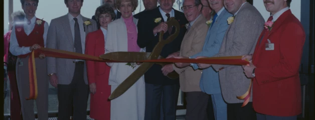 Group of people in business attire gathered for a ribbon cutting ceremony.