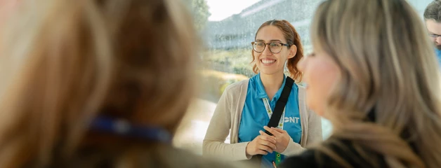 A person with glasses gesturing while speaking to others in a small group discussion.