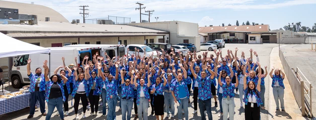 Large group of people in blue shirts gathered outdoors at what appears to be an industrial facility.