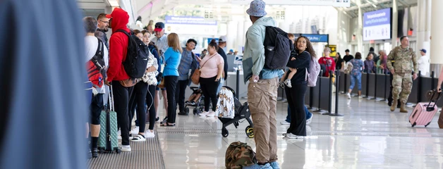 Travelers with luggage waiting in line at an airport terminal.