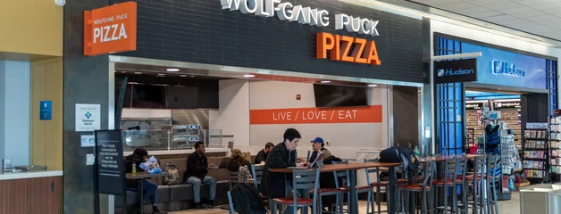 A food court pizza restaurant with seating area and customers inside a shopping mall.