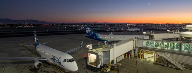 Aircraft at airport gate during sunset with colorful sky in background.