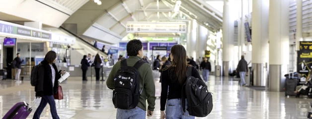 Travelers with luggage walking through Ontario International Airport terminal with high ceilings.