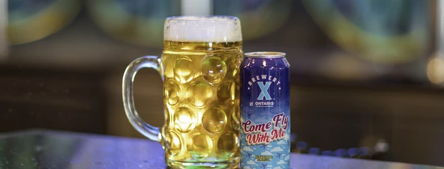 Photo of mug next to an branded aluminum can of the Come Fly With Me beer. 