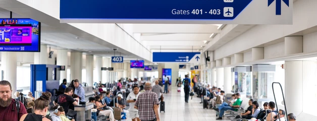 Busy airport terminal with passengers waiting and walking, departure signs above.