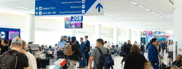 Airport terminal with travelers walking near blue directional signs and gates