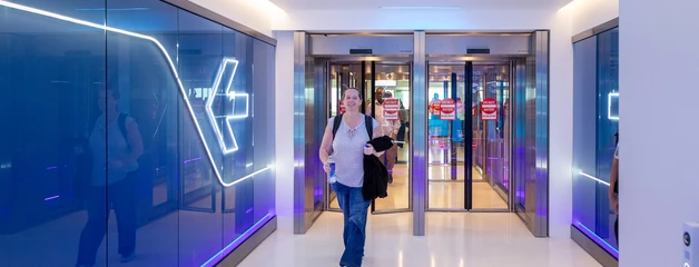Modern exit corridor with blue glass walls and people walking through.