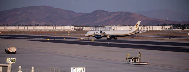 Large commercial aircraft on airport tarmac with mountains in background at dusk