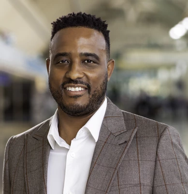 Jamal Avilez in gray suit jacket with blurred office background.