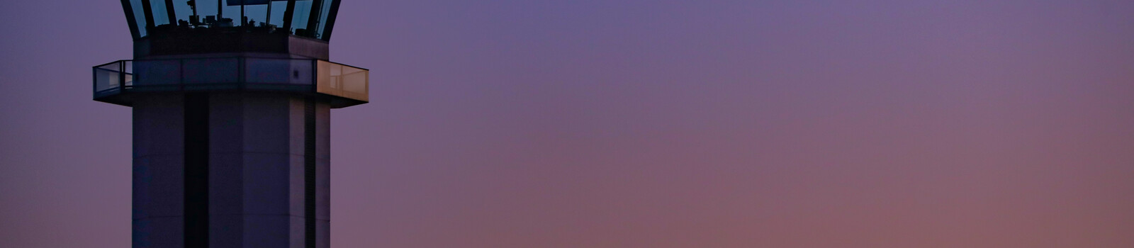 Air traffic control tower silhouetted against a purple sunset sky.