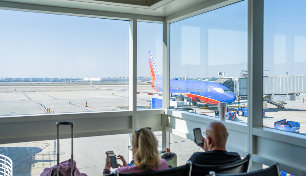 Airport terminal with people seated near large windows overlooking planes on the tarmac.