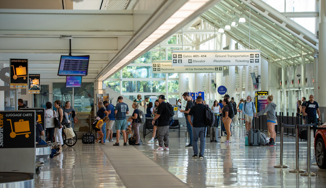 Travelers in bright airport terminal with glass roof and check-in counters.