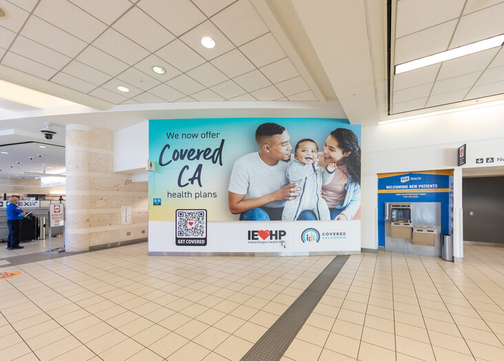 Airport terminal with a large advertisement banner hanging from the ceiling showing a blue promotional display.