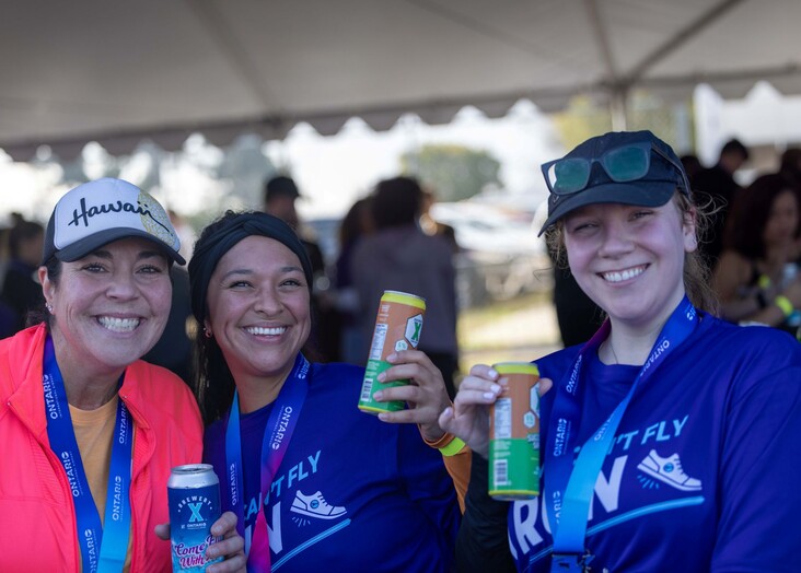 Three female runners toast Brewery X beers in the biergarten after the 5K at the Runway.